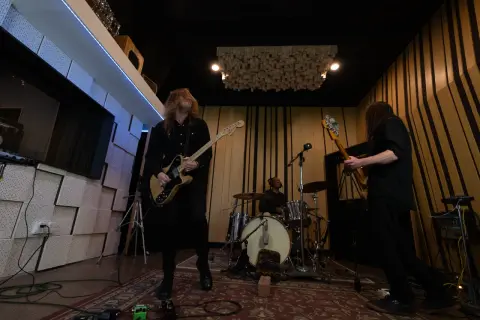Zakk Cervini and his band rock out in a studio, with a guitarist in the foreground, a bassist to the right, and a drummer in the background.