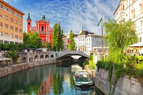Lublana atrakcje: rzeka Ljubljanica, Most Potrójny, kościół Franciszkanów i łódź wycieczkowa.