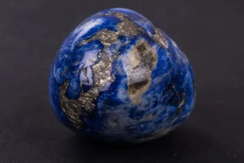 Un œuf en lapis-lazuli, rappelant les noces de saphir pour 56 ans de mariage, scintille de reflets dorés sur fond sombre.