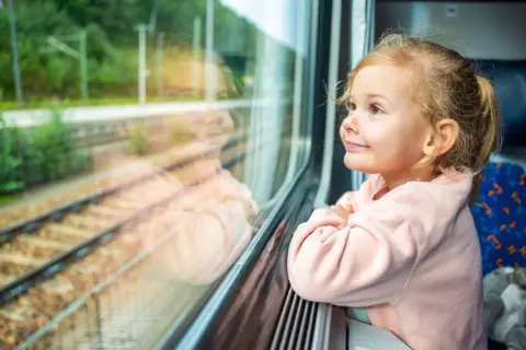 Uśmiechnięta dziewczynka w różowej bluzie patrzy przez okno pociągu. Czeka ją podróż pociągiem nad morze, a krajobraz za oknem już ją zachwyca.