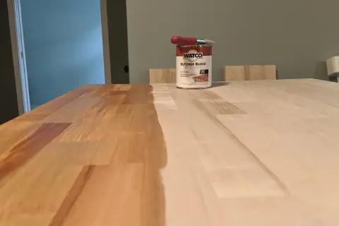 A can of Watco Butcher Block Oil & Finish sits on a wooden surface, with one half of the butcher block already stained and the other half awaiting treatment.