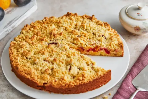 Ein saftiger Streuselkuchen mit Obst, bedeckt mit goldbraunen Streuseln, wartet darauf, angeschnitten zu werden.