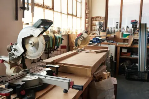 Un atelier menuiserie maison avec des scies circulaires, des établis et des outils. Des planches de bois sont prêtes pour être travaillées.