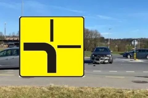 Znak drogowy informuje, kto ma pierwszeństwo na skrzyżowaniu równorzędnym. Widać uszkodzone auto po wypadku.