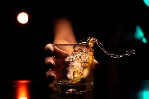 Dłoń trzyma szklankę z whisky, gdy płyn rozlewa się, tworząc falę. Kto wydaje koncesję na alkohol, by móc cieszyć się takimi chwilami?