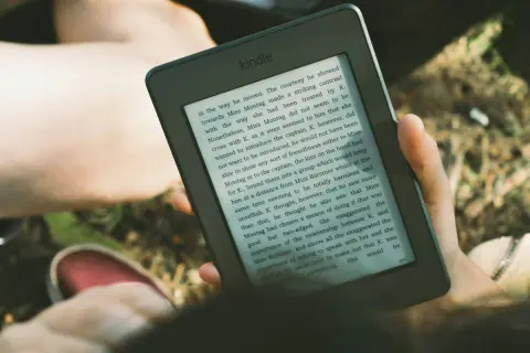 Osoba czyta książkę na czytniku Kindle, korzystając z Legimi.