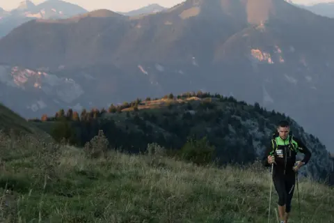 Un coureur en plein effort, bâtons en main, sur un sentier de montagne. Un aperçu de son plan d'entraînement UTMB.