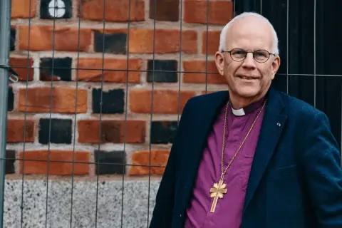 Biskop Marianne Langby Modéus ler mot kameran, klädd i en lila skjorta och en mörk kavaj. En guldkorshalsband hänger över hennes bröst.