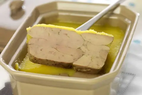 Tranche de foie gras au porto blanc, servie dans un plat en céramique avec une cuillère.