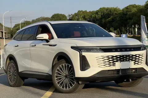 Biały OMODA 9 Super Hybrid z czerwonym wnętrzem stoi na drodze, z drzewami i budynkami w tle.