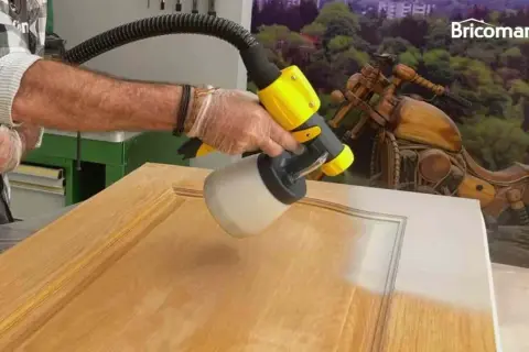 Hombre pintando una puerta de madera con una pistola pulverizadora. El resultado es un acabado liso y uniforme.