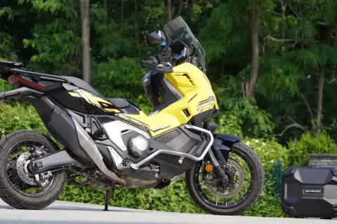 Żółty Honda X-ADV 750 z czarnymi akcentami, gotowy na przygodę. Obok bagażnik kufer.