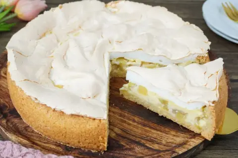 Ein saftiger Rhabarberkuchen mit Baiserhaube, ein Stück davon ist angeschnitten und zeigt die cremige Füllung.