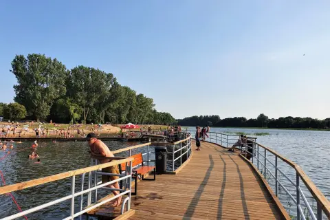 Ludzie odpoczywają i kąpią się nad zalewem Borki Radom. Drewniane molo zaprasza do spacerów i podziwiania widoków.