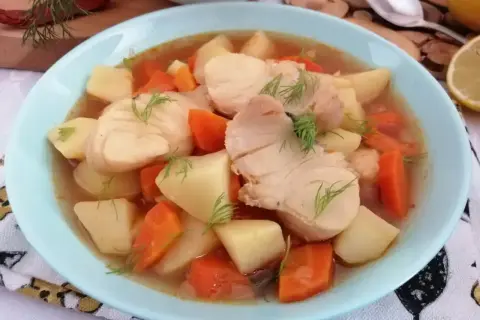 Miska zupy rybnej z kawałkami ryby, ziemniaków i marchewki, udekorowana koperkiem.