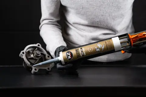 Osoba w czarnych rękawiczkach aplikuje czarny silikon z pistoletu na część pompy wodnej.