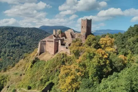 Les 3 châteaux de Ribeauvillé, perchés sur une colline boisée, se dressent fièrement sous un ciel bleu parsemé de nuages.