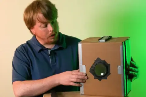 Mężczyzna pokazuje, jak zrobić camera obscura z kartonu. Prosty projekt DIY.