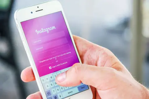 Dłoń trzyma smartfon z ekranem logowania Instagram. Dowiedz się, jak dodać zdj na Insta, logując się lub tworząc konto.