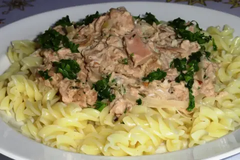 Pyszny makaron z tuńczykiem, posypany świeżą natką pietruszki, podany na białym talerzu.