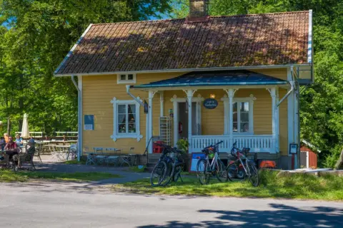 Gult hus med café & vandrarhem. Cyklar står parkerade framför. Folk sitter vid bord utomhus.