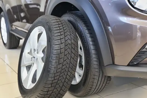 Dwa opony samochodowe, jeden całoroczny, drugi zimowy, obok brązowego samochodu.