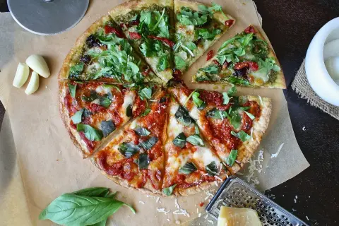 Pizza podzielona na pół: jedna połowa z pesto i rukolą, druga z sosem pomidorowym i bazylią.
