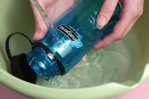 Hände spülen eine blaue Nalgene-Flasche mit kochendem Wasser in einer grünen Schüssel.