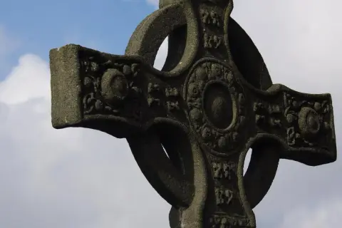 Kamienny krzyż celtycki z misternymi zdobieniami na tle błękitnego nieba z chmurami.