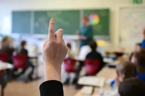 Ein Schüler hebt die Hand im Unterricht. Seit wann gibt es die Schulpflicht in Deutschland? Die Antwort liegt im Dunkel der Geschichte, aber die heutige Schulpflicht ist ein Meilenstein.