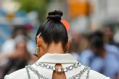Capelli raccolti in un elegante chignon alto, impreziositi da una collana scintillante su un abito bianco.