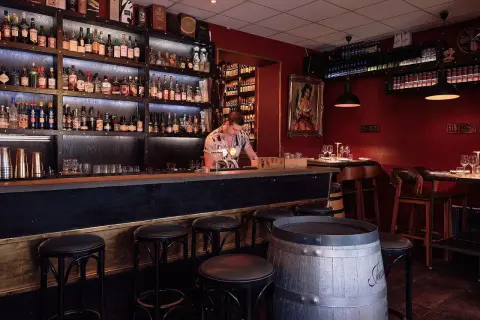 En bar med hyllor fyllda med flaskor, en bardisk med pallar och en bartender. En perfekt plats för vinbarer Stockholm.