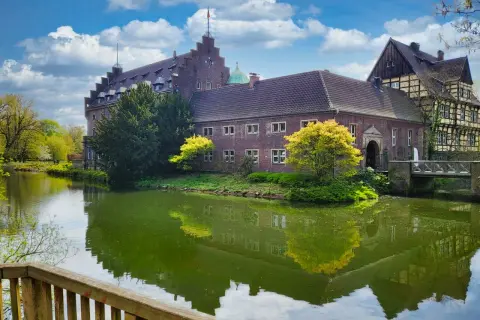 Schloss Wittringen, ein imposantes Backsteingebäude, spiegelt sich im Wasser eines umliegenden Grabens.