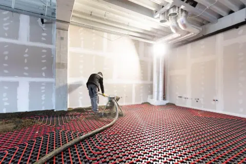 Un ouvrier installe un système de chauffage par le sol électrique, avec des tuyaux rouges sur une grille noire.