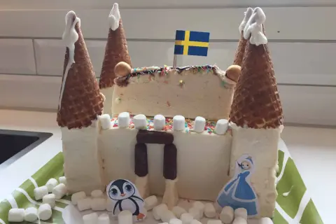 En fantasifull glasstårta formad som ett slott, perfekt för barn. Med svenska flaggan på toppen och dekorerad med marshmallows, strössel och söta figurer.