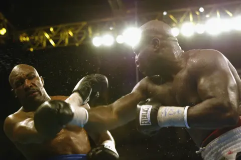 Two boxers clash under bright lights. The sound of their punches echoes, a testament to the force behind each blow.