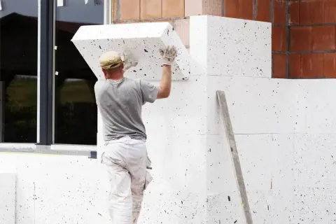 Pracownik montuje styropian na ścianie domu. Zastanawiasz się, ile kosztuje ocieplenie domu 200m2?
