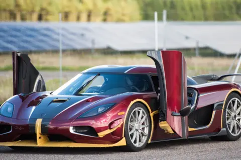 Czerwony Koenigsegg Agera RS z otwartymi drzwiami, gotowy do startu na tle paneli słonecznych.