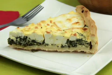Rebanada de quiche de espinacas con queso feta y una corteza dorada, lista para ser disfrutada.