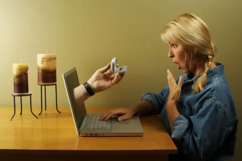 Zaskoczona kobieta otrzymuje pierścionek zaręczynowy przez ekran laptopa. To nowa historia domeny miłości.