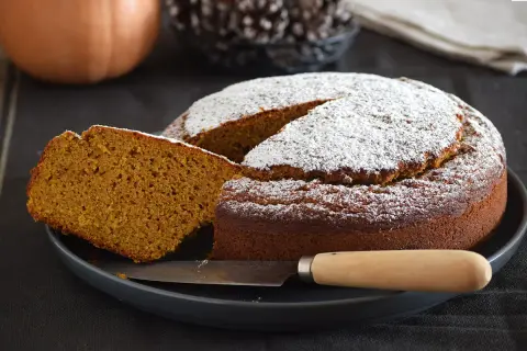 Un delicioso bizcocho de calabaza espolvoreado con azúcar glas, con una rebanada cortada y un cuchillo listo para servir.