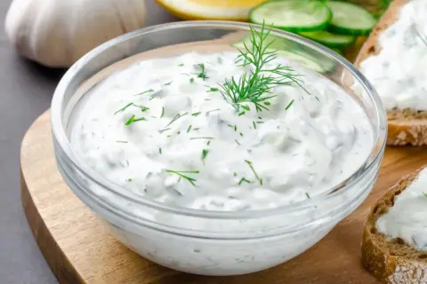 Un bol de salsa de yogur con eneldo y pepino, listo para untar en pan tostado.