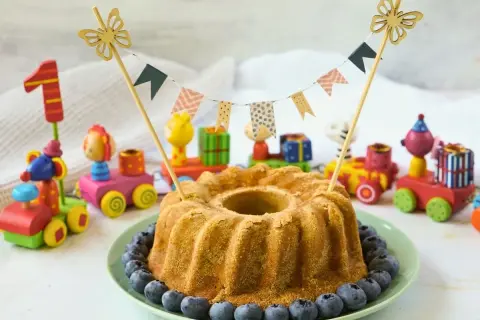 Saftiger Kuchen ohne Zucker für Kinder, dekoriert mit Blaubeeren und bunten Holzspielzeugen. Perfekt für den ersten Geburtstag!