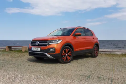 Pomarańczowy Volkswagen T-Cross stoi nad jeziorem, gotowy na letnią przygodę.