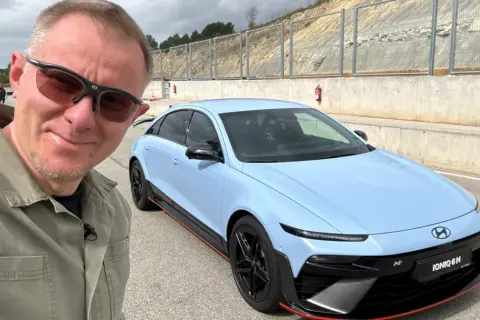 Mężczyzna w okularach przeciwsłonecznych pozuje do selfie z błękitnym Hyundaiem IONIQ 6 N na torze wyścigowym.