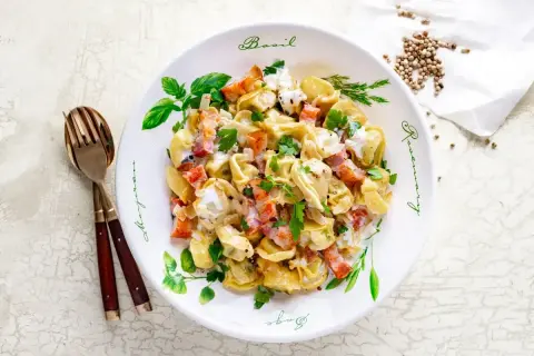 Pyszne tortellini z boczkiem i śmietanowym sosem, idealne jako pomysł na obiad. Posypane natką pietruszki.