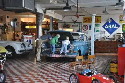 Familie inspiziert blauen Oldtimer in Werkstatt. Die Restaurierung des Autos scheint ein gemeinsames Projekt zu sein.