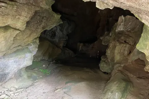 Entrada a la cueva de la Loja, con rocas irregulares y un camino de tierra que se adentra en la oscuridad.