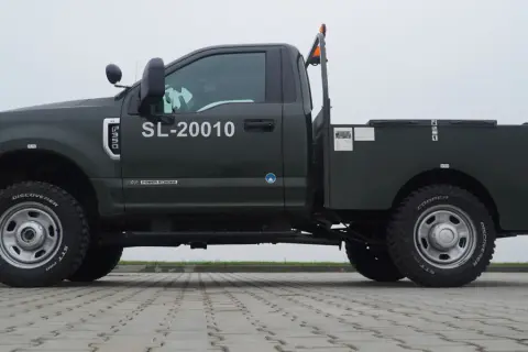 Ciemnozielony Ford F350 z platformą, numerem SL-20010 i pomarańczowym kogutem na dachu.