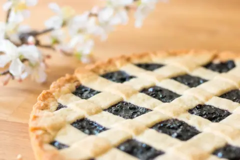 Ein köstliches Crostata-Rezept mit Blaubeerfüllung und Gittermuster, daneben zarte weiße Blüten.